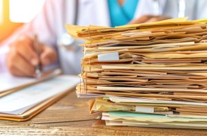 A close-up of a large stack of medical files on a wooden desk suggesting the need for digitization.